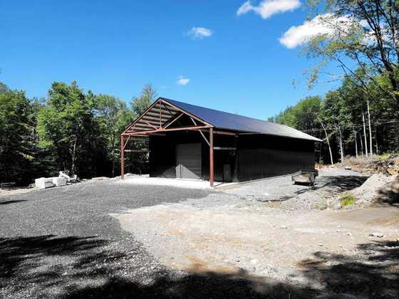 The shop building and its steel canopy on the gravel yard, among the trees