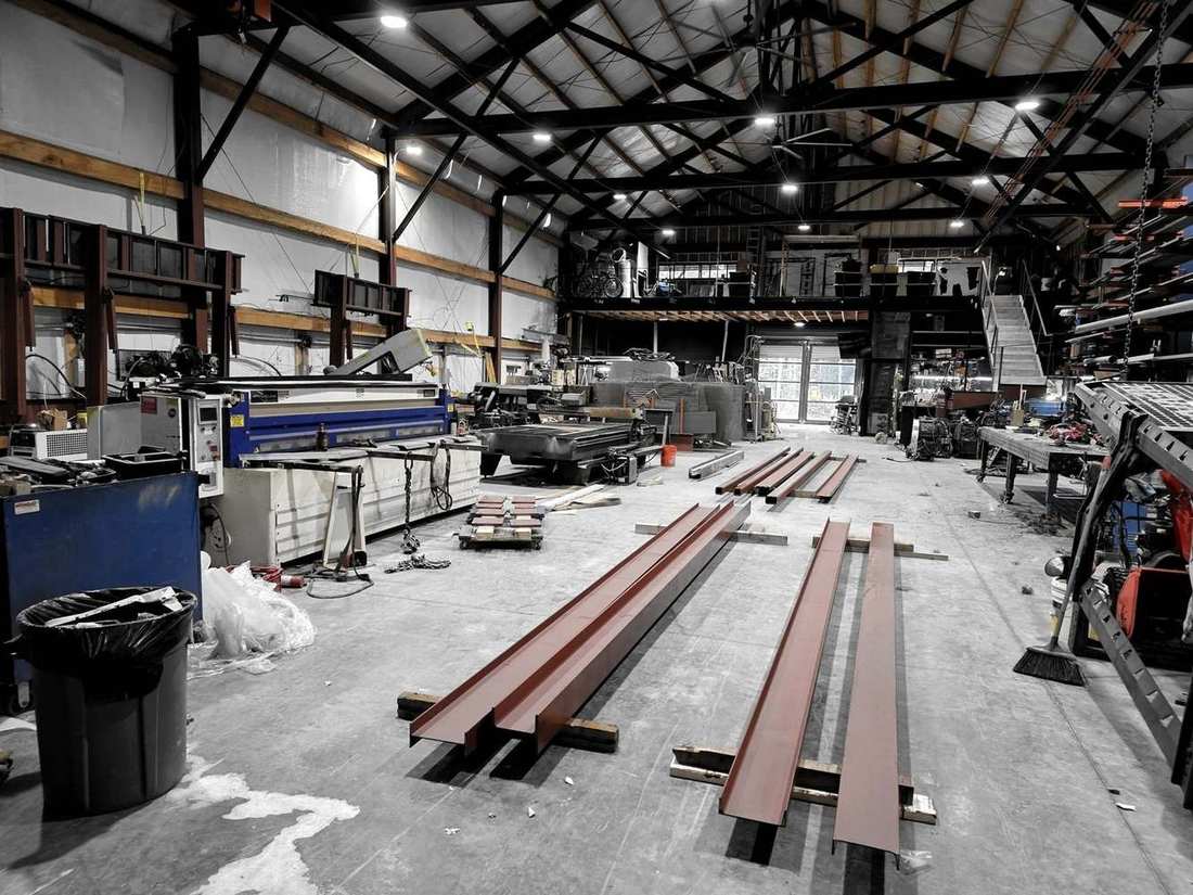 Wide view of the Ellenville shop interior with red-primed beams laid out under the trusses