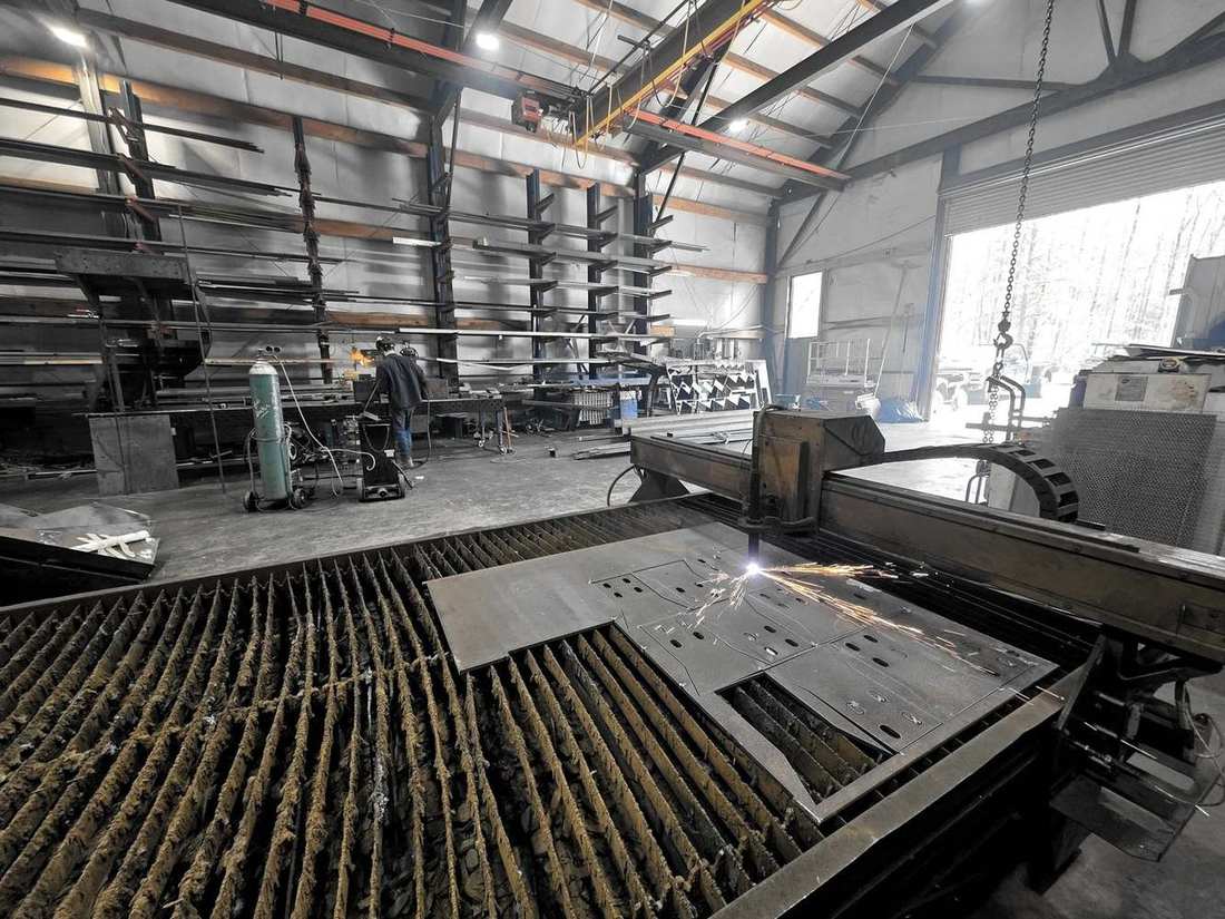 CNC plasma cutting a plate, sparks across the table, steel racks behind